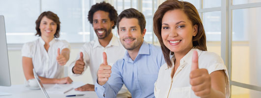 Cuatro personas sonriendo y haciendo el gesto de pulgar hacia arriba en una oficina